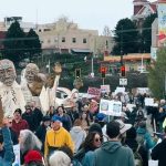 Thousands of protesters march through downtown Bellingham, Washington, during the No Kings Day of Action on March 28, 2026, carrying signs and large puppet figures