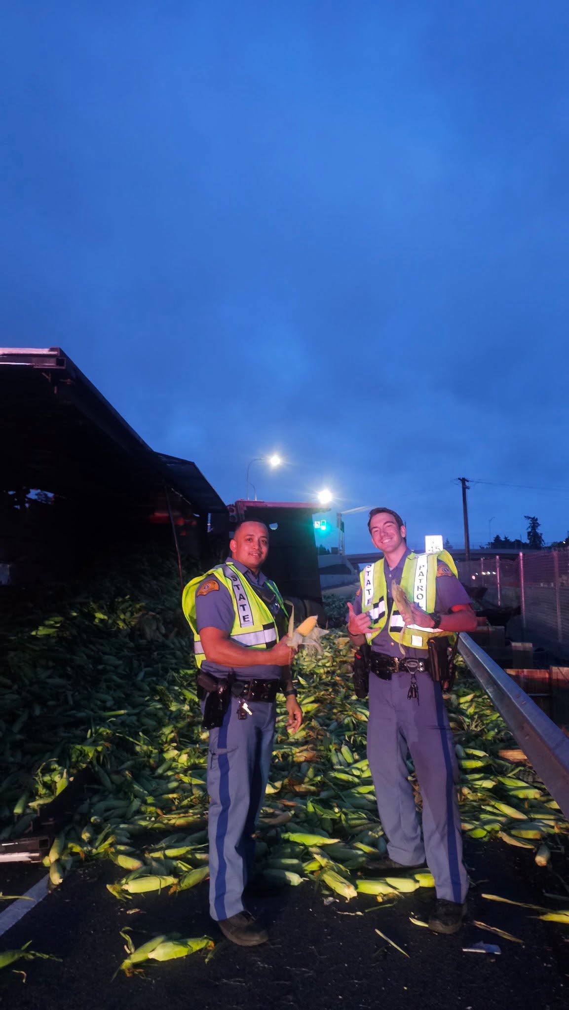 Washington State Patrol troopers stand near the spilled corn at the crash scene