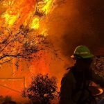 A firefighter battles flames threatening a home during the wildfire crisis burning across Eastern Washington.