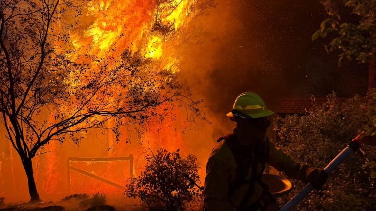 A firefighter battles flames threatening a home during the wildfire crisis burning across Eastern Washington.