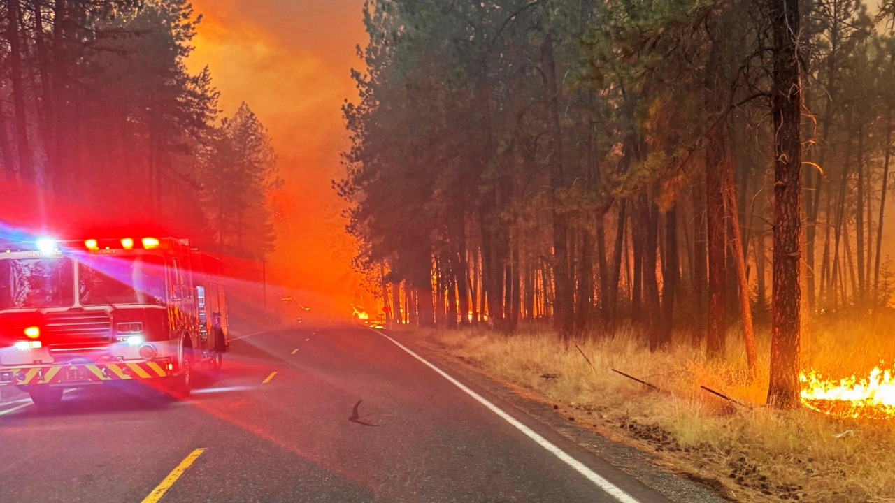 A Spokane Valley Fire Department engine operates as flames burn through timber along a Spokane-area roadway during the Spokane Complex fires. Photo courtesy of Spokane Valley Fire Department