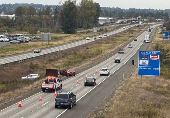 A Washington State Patrol trooper and WSDOT incident response crew work the scene along northbound I-5 as traffic passes by. A separate vehicle was also pulled over by WSP in the area at the time.