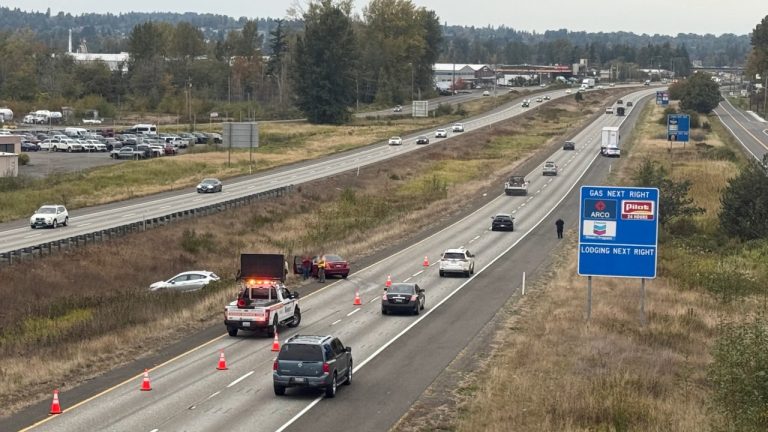 A Washington State Patrol trooper and WSDOT incident response crew work the scene along northbound I-5 as traffic passes by. A separate vehicle was also pulled over by WSP in the area at the time.